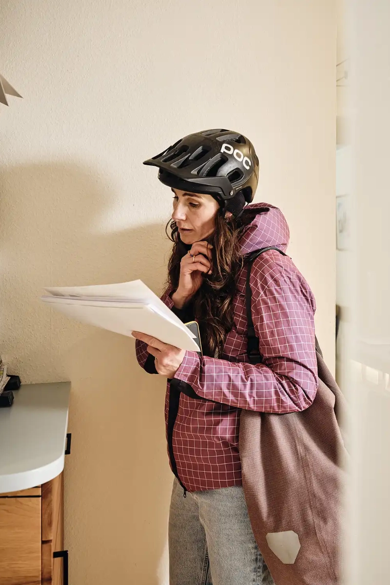 Eine Frau mit Fahrradhelm ist gerade im Büro angekommen und öffnet Post